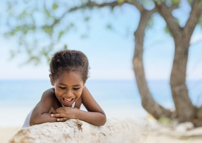 Fijian girl watching crab walk across log on beach.