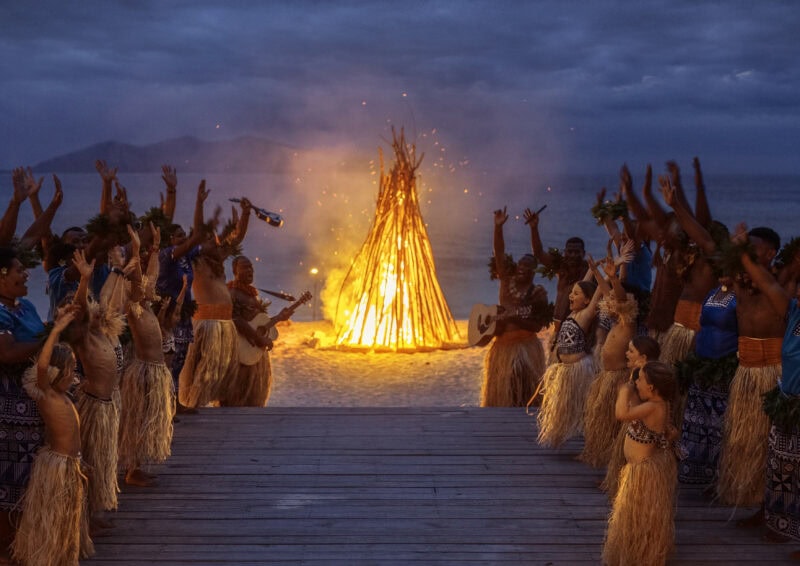 Meke group celebrating next to bonfire on beach.